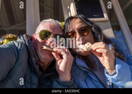 happy middle aged couple in love taking a selfie while eating a snack in an outdoor pub Stock Photo