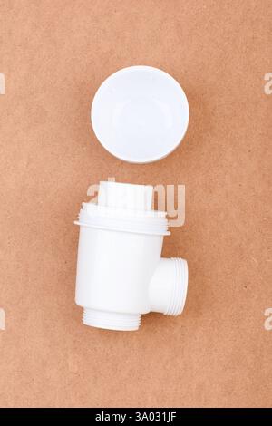 White plastic sink drain trap with threaded ends and open plug placed on brown surface. Stock Photo