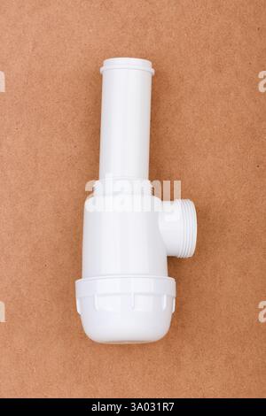 White plastic sink drain trap with threaded ends and overflow pipe placed on brown surface. Stock Photo