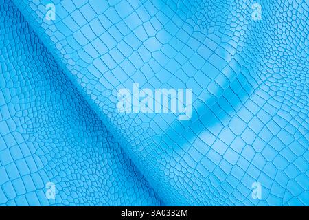 Blue color crocodile skin artificial leather with waves and folds on PVC base. Stock Photo