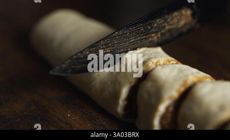 Cinnamon Roll Making: Slicing the dough log into pieces with a knife. Stock Photo