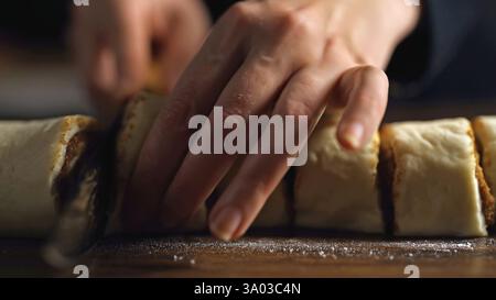 Cinnamon Roll Making: Slicing the dough log into pieces with a knife. Stock Photo