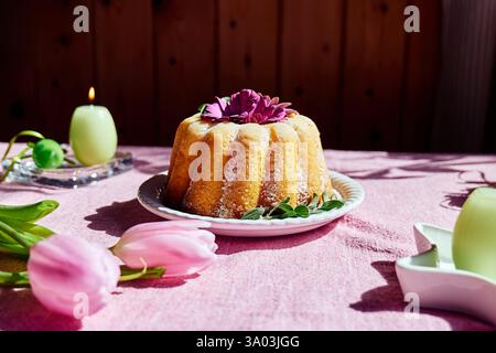 Easter cake decorated with icing sugar and daisy flowers on the table with easter eggs and tulips on  pink tablecloth. Traditional easter cake or swee Stock Photo