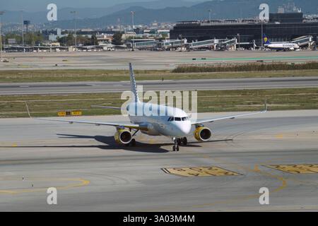 Full image of white jet airplane parked on tarmac at large airport with runway and terminal in background. Stock Photo