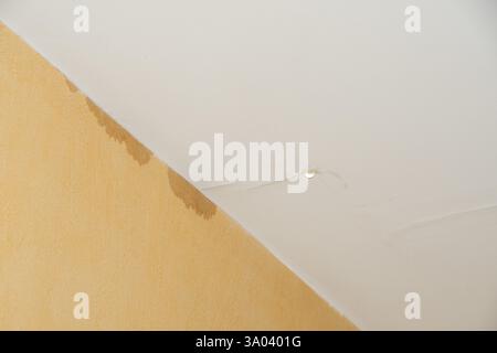 Water damage on ceiling with visible stains and crack in yellow interior Stock Photo