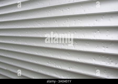 Hail marks create texture on metal roller shutter  after severe weather event Stock Photo