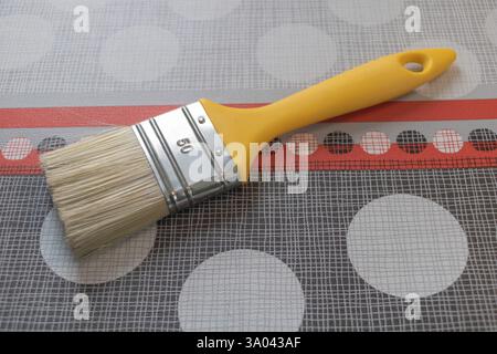 Paintbrush with a yellow handle on top of a paper grid, with a background of red and white stripes and large gray circles. Stock Photo