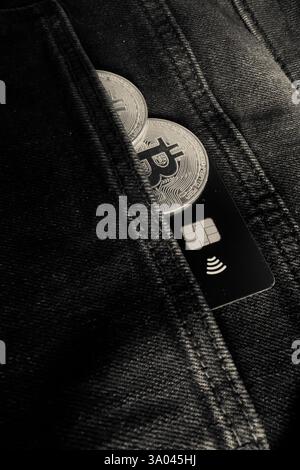 Credit card next to two Bitcoin physical coins inside a black jeans pocket Stock Photo