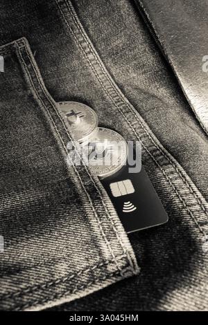 Credit card next to two Bitcoin physical coins inside a black jeans pocket Stock Photo
