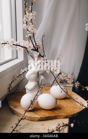 Beautiful branches lie on a wooden board on the windowsill. Composition with Easter eggs and bunny. Spring greeting background with place for text. Stock Photo
