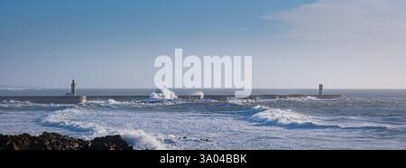 A lighthouse and a concrete pier on the shore of a raging ocean. Huge waves crash against the walls, creating an explosion effect. White foam and spra Stock Photo