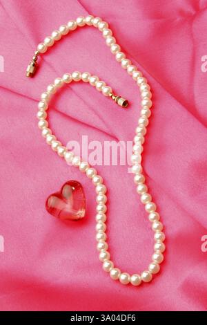 Jewellery in form pearl necklace with synthetic red gem stone of heart shape against pink satin background Stock Photo