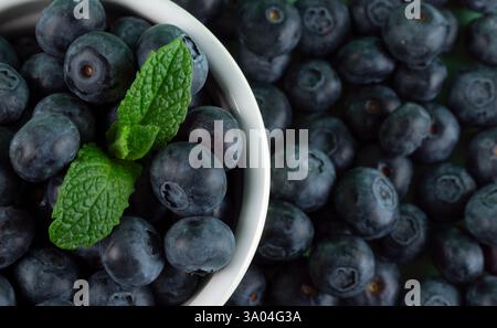 A bowl of blueberries with a green leaf in the middle and a lot of blueberries in the background. The blueberries are fresh and ripe, and the leaf add Stock Photo