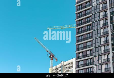 Under construction multistory building in downtown metropolis. Crane working on unfinished concrete facade of modern high-rise condominium. Clear blue Stock Photo