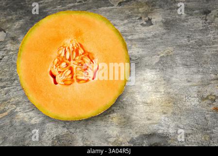 A freshly cut Cantaloupe half with seeds on a slate table top, with copy space. Stock Photo