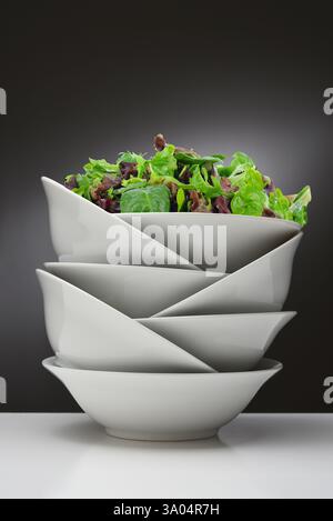 A leafy green salad in the top bowl of a stack of white china bowls. Stock Photo