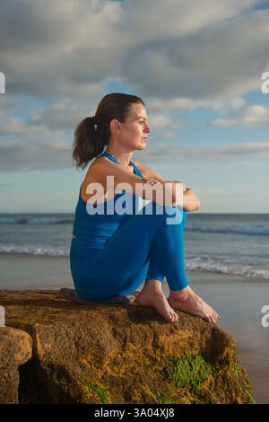 sporty woman sitting on a rock by the ocean looking at the view Stock Photo