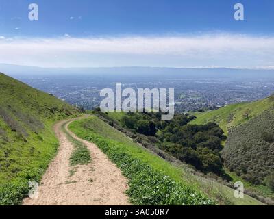 A dirt trail winds through vibrant green hills of Sierra Vista Open Space Preserve. The view of Silicon Valley urban sprawl. Stock Photo