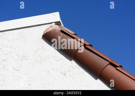 A roof corner with weathered clay tiles and white stucco siding. Stock Photo