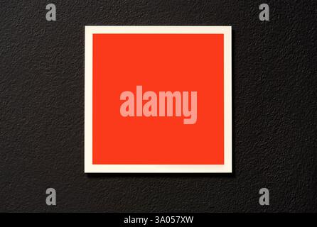 Blank red square label sticker on a black wall indoors, empty framed warning sign template, white border minimal frame sign template, symbol copy spac Stock Photo