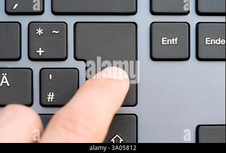 Finger pressing a simple blank enter key on a computer keyboard, empty button with copy space for text or a symbol, close-up. Modern workspace, enter Stock Photo