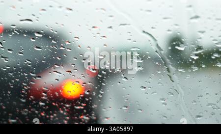 Raindrops on front car window, inside view during rainy stormy weather, blurred road and vehicle in background, rain on windshield while stationary, w Stock Photo