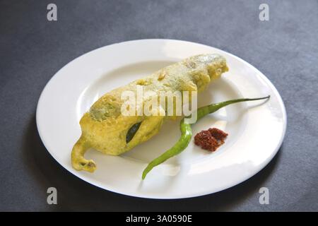 Indian fast food fried chilli vada mirchivada with red chutney and green chilli served in plate on black background Stock Photo