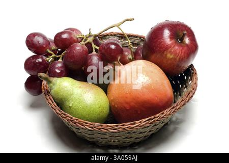 Fruits, water drops on apple, pomegranate, pear and grapes in wooden basket on white background Stock Photo