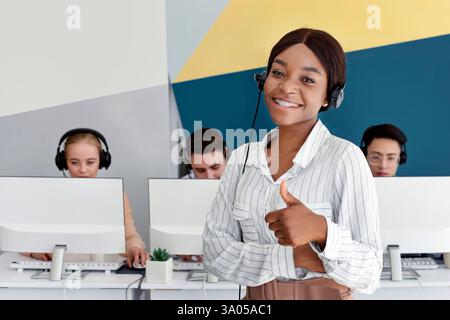 Black female hotline operator smiling and showing thumb up at modern call centre Stock Photo