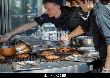 Professional cooks grilling delicious steaks and mushrooms for customers in a commercial kitchen. Moscow, Russia June 20, 2018 Stock Photo