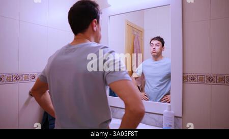 Sleepy man looking at mirror in bathroom before work Stock Photo