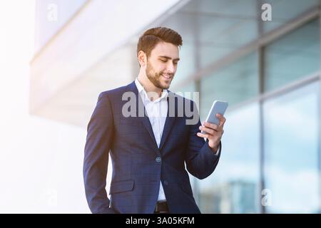 Successful young enterpreneur using cellphone for online communication near government office Stock Photo