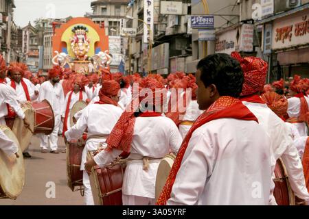 Indian girls and men wearing red colored headgear called feta and white kurta pajamas and playing musical instrument called 'dhol' during immersion fe Stock Photo