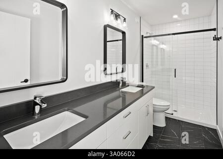 Bathroom with a large mirror and two sinks. The mirror is framed in black and the sink is white. The bathroom has a modern and sleek design Stock Photo