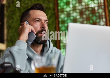 Thoughtful young adult man in casual clothes in cafe talking on a mobile phone Stock Photo