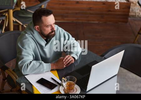 Serious bearded man in casual clothes in cafe using his laptop Stock Photo