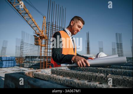 In orange colored uniform. Man is working on the construction site at daytime. Stock Photo