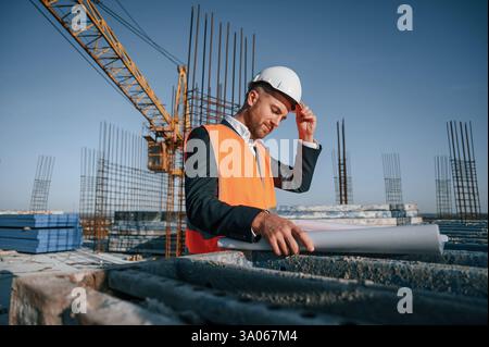 In orange colored uniform. Man is working on the construction site at daytime. Stock Photo