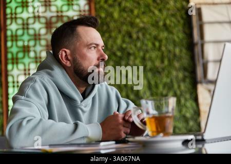 Serious bearded man in casual clothes in cafe using his laptop Stock Photo