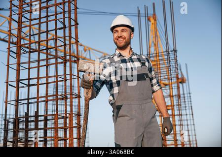 With big hammer in hands. Man is working on the construction site at daytime. Stock Photo