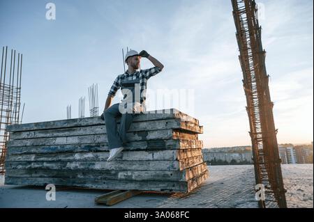 Sitting and looking to the side. Man is working on the construction site at daytime. Stock Photo