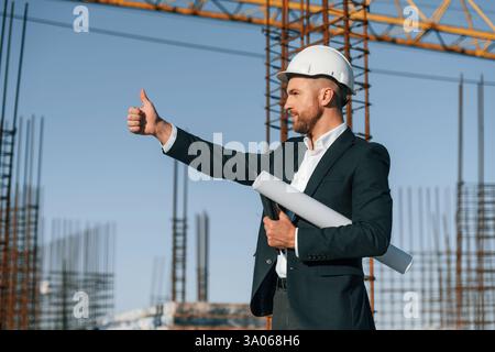 Showing thumb up. Businessman in formal clothes is on the construction site at daytime. Stock Photo