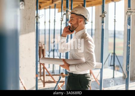 Using phone. Manager is in the formal clothes. Man is working on the construction site at daytime. Stock Photo