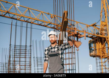 Against crane. With wooden plank. Man is working on the construction site at daytime. Stock Photo