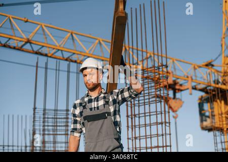 Against crane. With wooden plank. Man is working on the construction site at daytime. Stock Photo