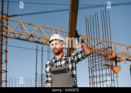 Against crane. With wooden plank. Man is working on the construction site at daytime. Stock Photo