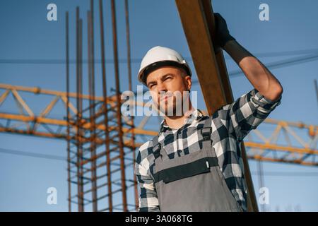 Against crane. With wooden plank. Man is working on the construction site at daytime. Stock Photo