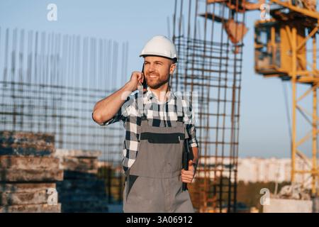 Beautiful man is working on the construction site at daytime and talking by phone. Stock Photo
