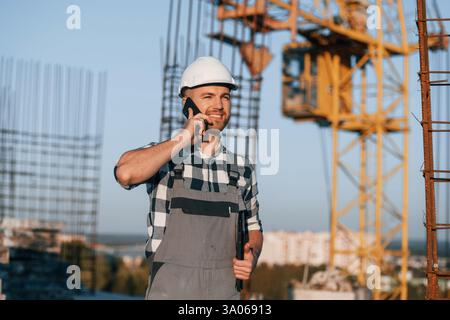 Beautiful man is working on the construction site at daytime and talking by phone. Stock Photo