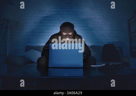 Masked hacker downloading private information using pc Stock Photo